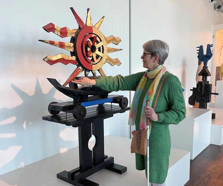 Dame med blindestokk som tar på skulptur