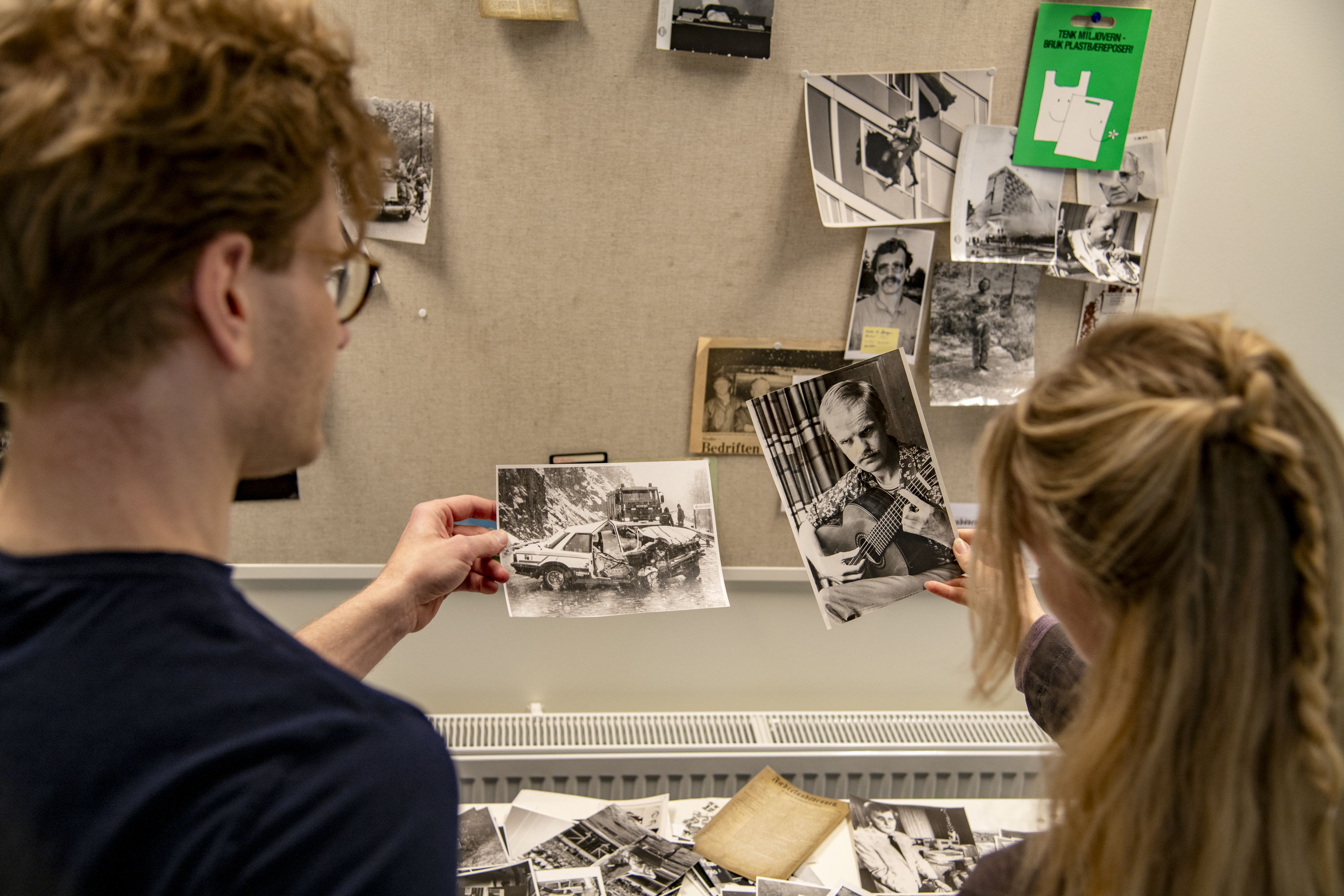 Bilde av to personer bakfra som holder opp gamle fotografier. 