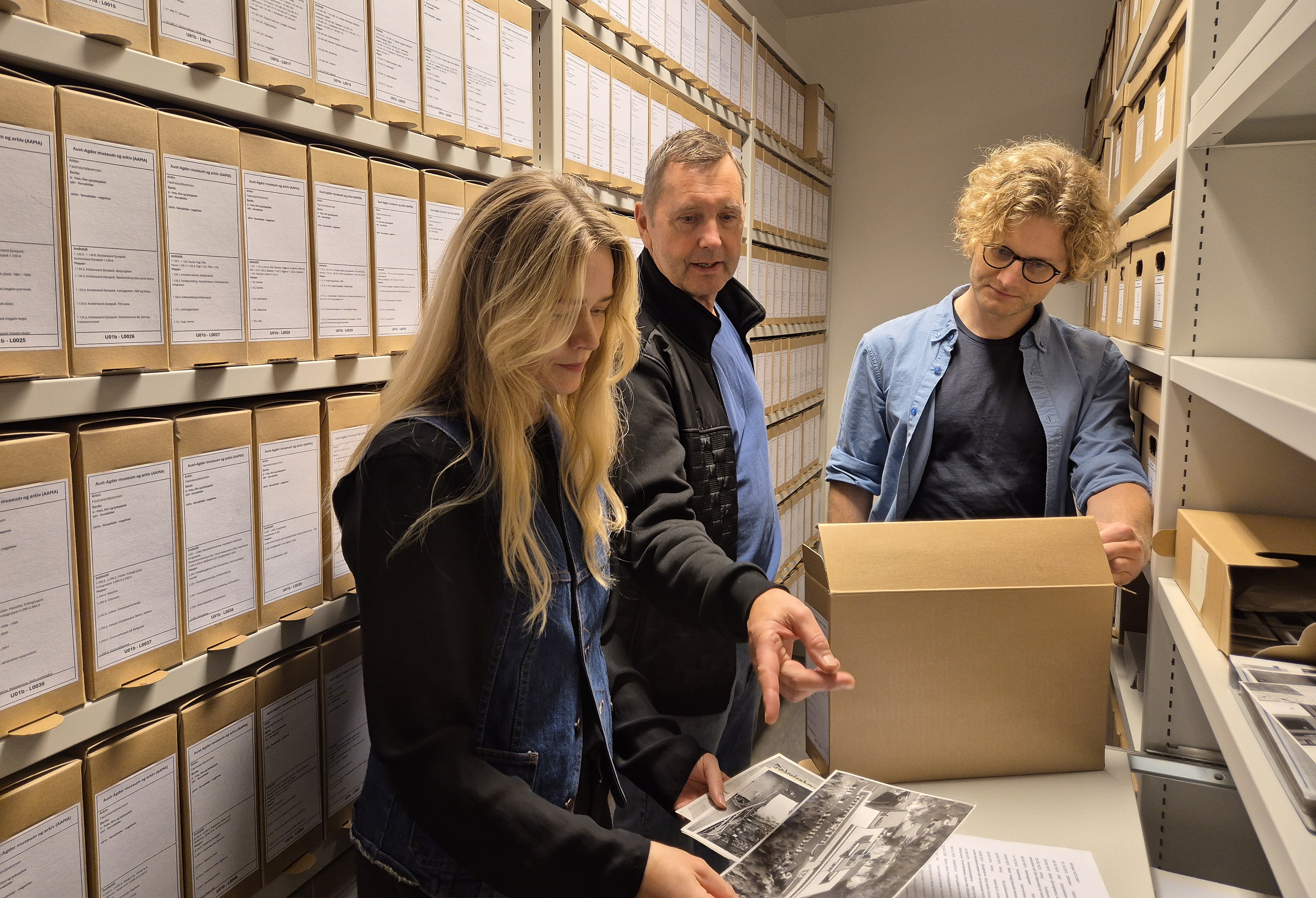 Tre personer mellom hyllene i magasin