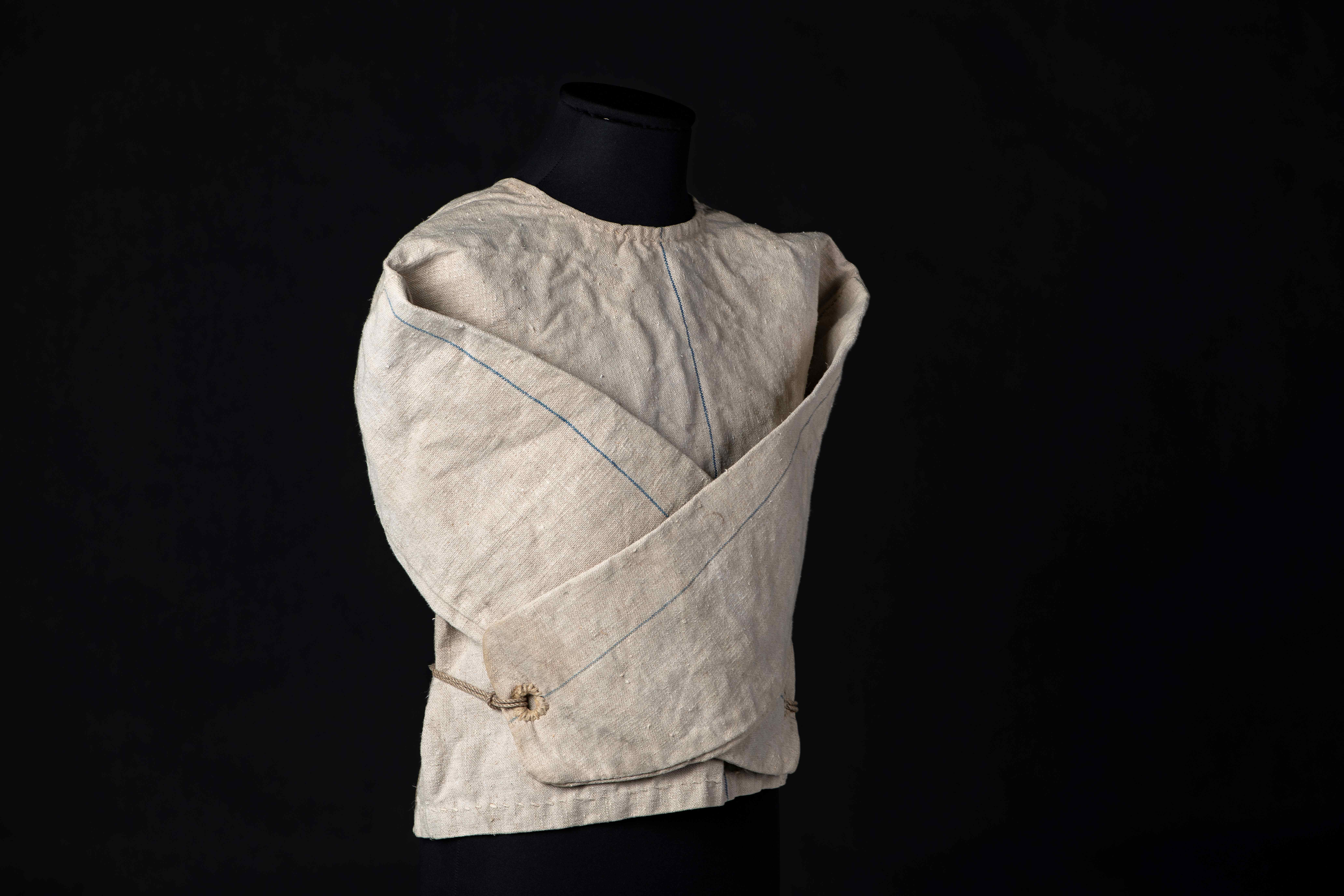 Bilde av et gammelt tøystykke der ermene er krysset og bundet